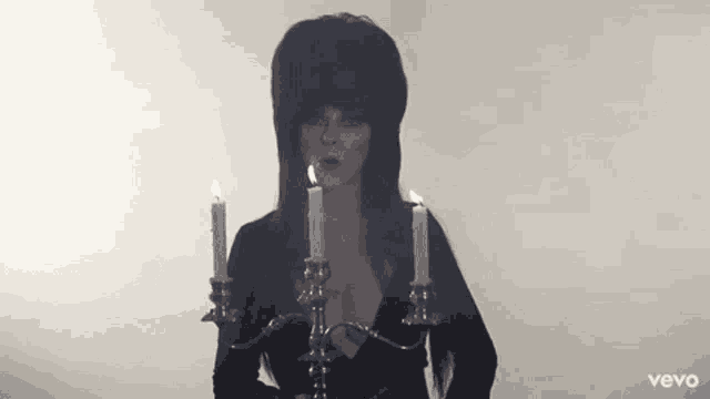 a woman in a black dress is holding a candle holder with candles .