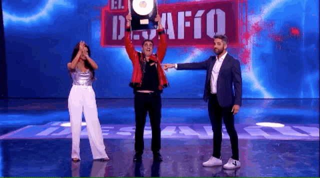 a man in a red jacket is holding a trophy in front of a sign that says " el desafio "
