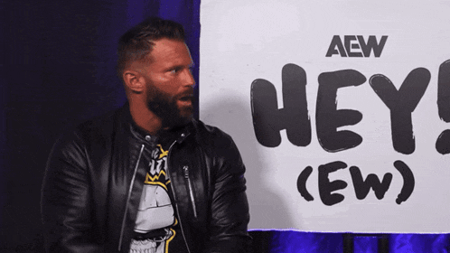 a man in a leather jacket is standing in front of a sign that says hey