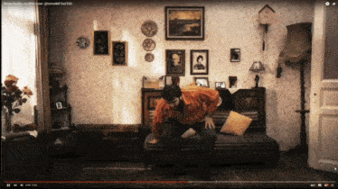 a man is sitting on a couch in a living room with a youtube video playing