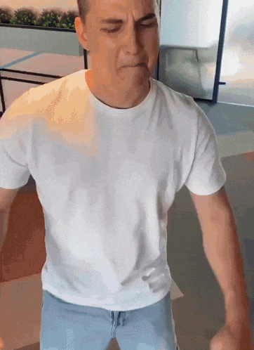 a man in a white t-shirt and blue jeans is making a funny face