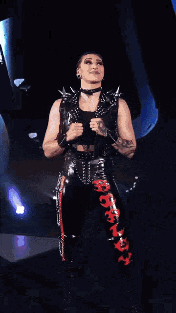 a woman in a black vest and red pants stands in front of a blue background