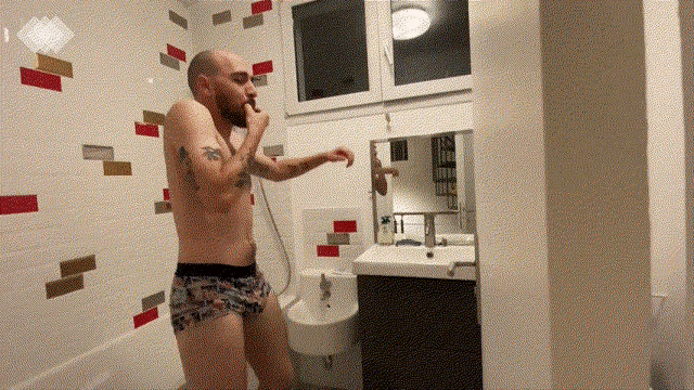 a shirtless man standing in a bathroom with a brick wall