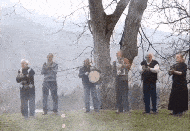 a group of people standing in a field with trees in the background