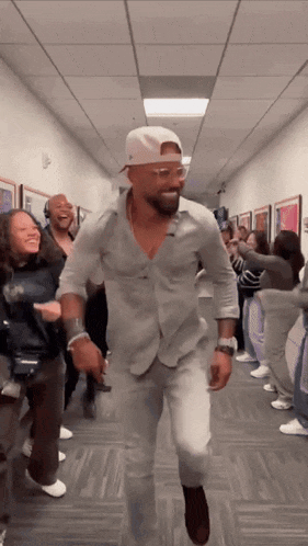 a man in a white hat is dancing in a hallway with people .