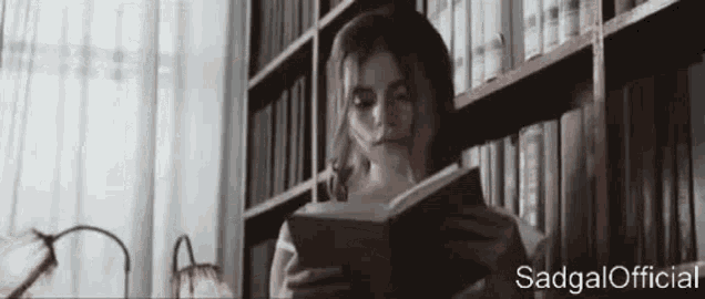 a woman is reading a book in a library while sitting in front of a bookshelf .