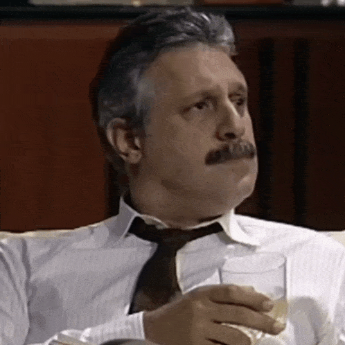 a man with a mustache is sitting on a couch and holding a glass