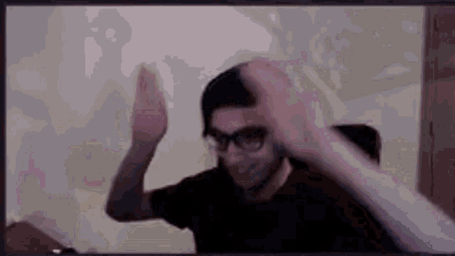 a man wearing glasses is giving a high five while sitting in front of a computer screen .