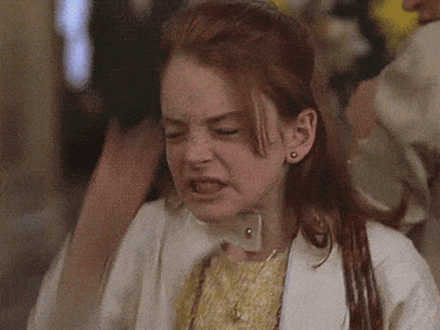 a young girl with red hair is making a funny face while wearing a white jacket and a yellow dress .