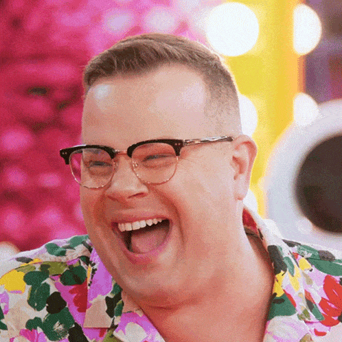 a man wearing glasses and a colorful shirt is laughing with his mouth open