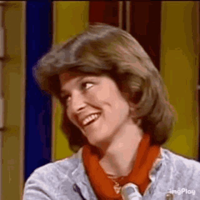 a woman is smiling and looking at the camera while sitting in front of a yellow wall .