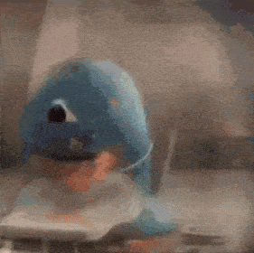 a blue stuffed animal is sitting on a table with a remote control in its mouth
