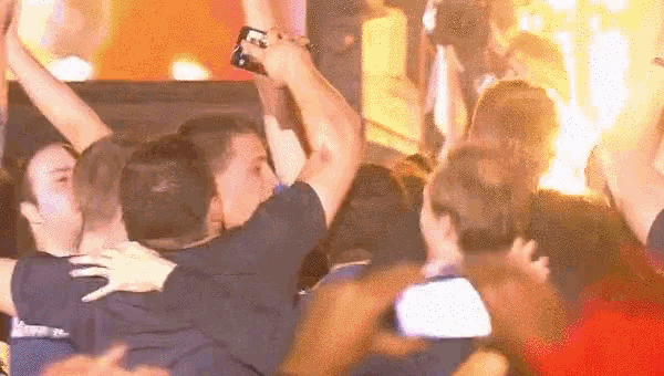 a group of people are celebrating with their arms in the air and one of them is holding a cell phone