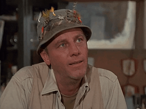 a man wearing a hat with feathers and fishing flies on it