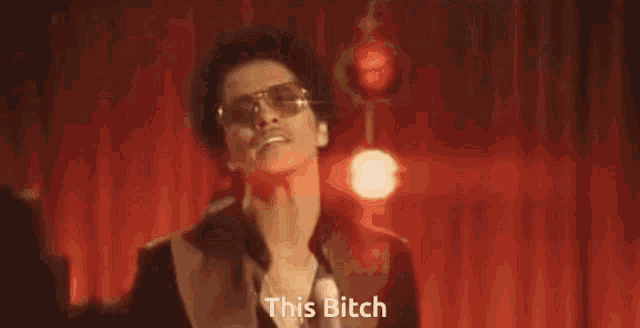 a man in a suit is singing into a microphone while a woman is laying on the floor and says this bitch
