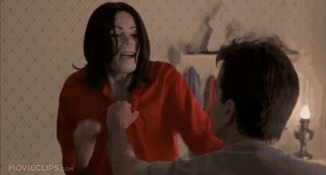 a woman in a red shirt is holding a man 's hand in a movie clip from movieclips.com