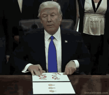donald trump is sitting at a desk signing a document that says " fuck you "