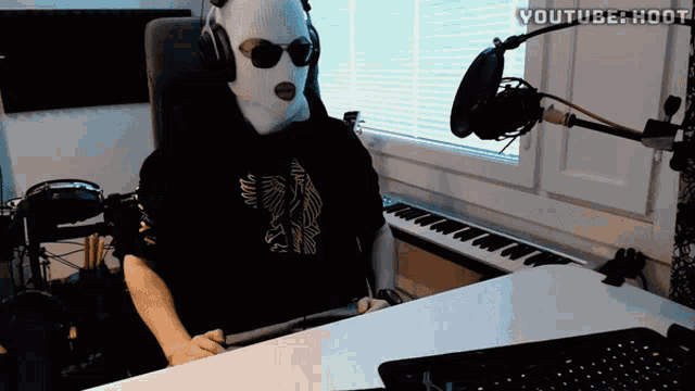 a man wearing a ski mask is sitting at a desk in front of a keyboard and microphone with youtube hoot written on the top