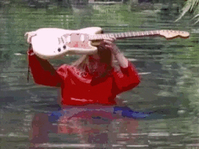 a man in a red shirt is holding a white electric guitar in the water .