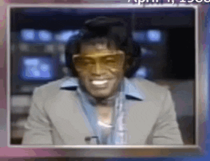 a man in a suit and sunglasses is smiling while wearing headphones and a microphone .