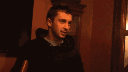 a man wearing a black hoodie is standing in front of a window