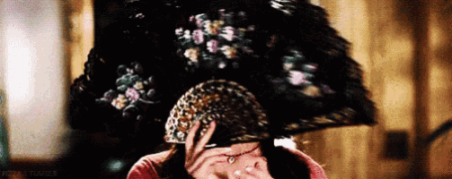 a woman is holding a large fan over her head .