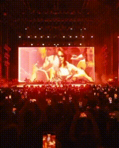 a crowd of people watching a concert with a large screen on the stage