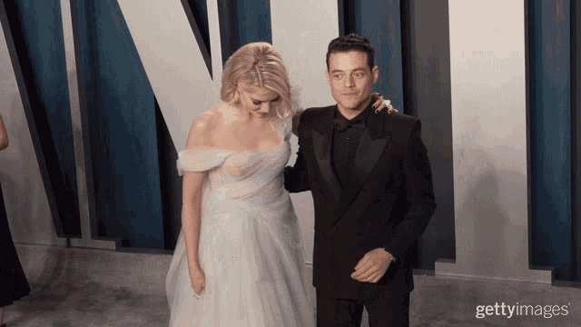 a man in a tuxedo and a woman in a white dress pose for a picture