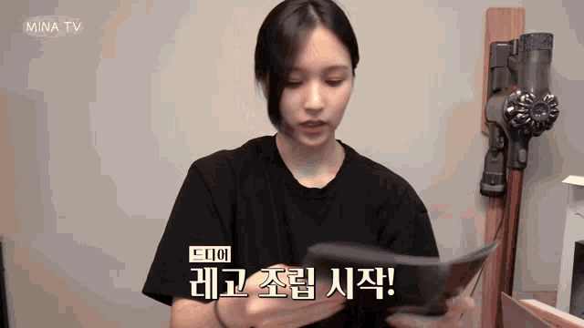 a woman is holding a book in front of a vacuum cleaner that says mina tv on it