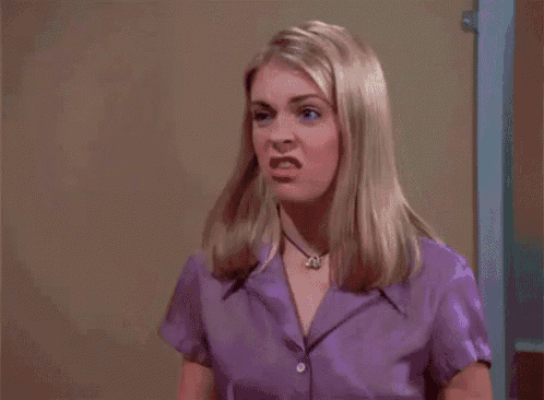 a blonde woman wearing a purple shirt and a necklace is standing in front of a door .
