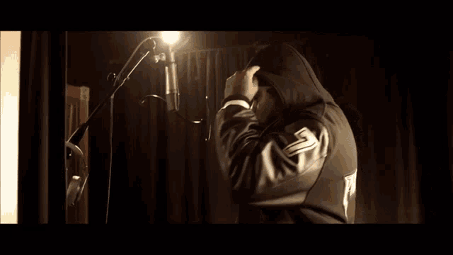 a man in a hooded jacket with the letter s on the back is standing in front of a microphone
