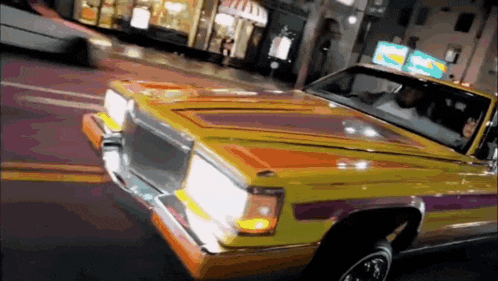 a yellow car with purple stripes is driving down a street .