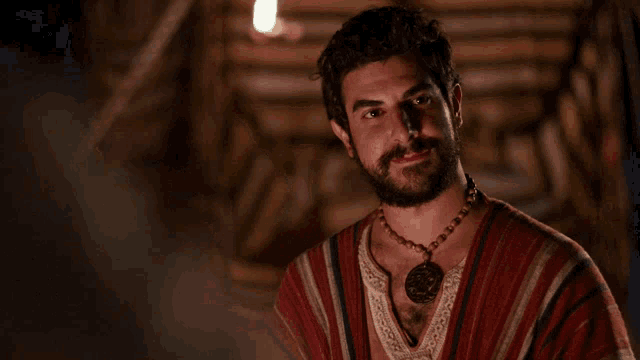 a man with a beard is wearing a striped shirt and a necklace with a pendant on it