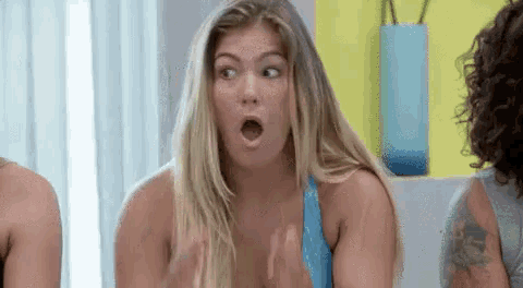 a woman in a blue tank top is making a surprised face while sitting in front of a group of women .