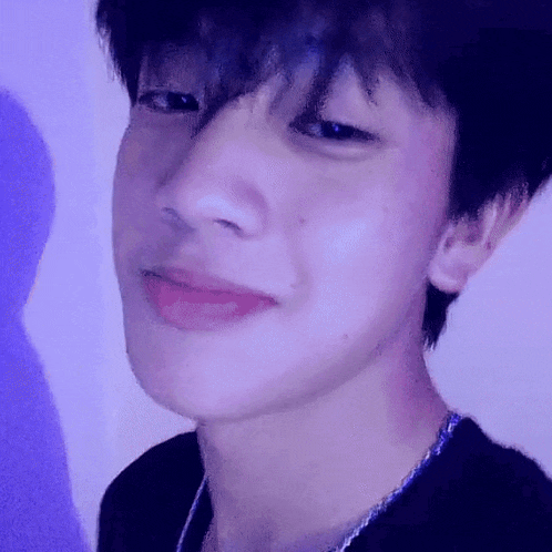 a close up of a young man 's face with a purple background and a necklace .