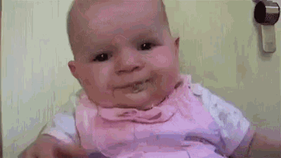 a baby in a pink dress is making a funny face while eating .