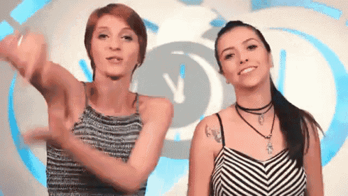 two women are dancing in front of a clock with the letter v on it .