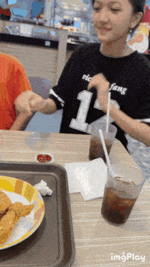 a girl wearing a black shirt with the number 1 on it sits at a table