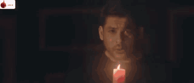 a man in a black shirt and red tie is standing in a dark room looking at something .
