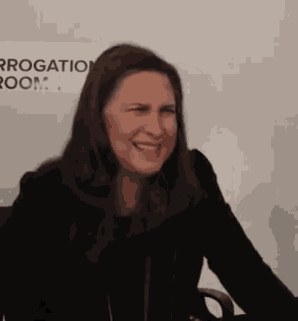 a woman in a black jacket is sitting in front of a sign .