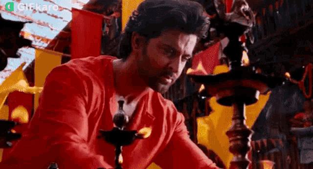 a man in a red shirt is sitting at a table with a lamp on it .