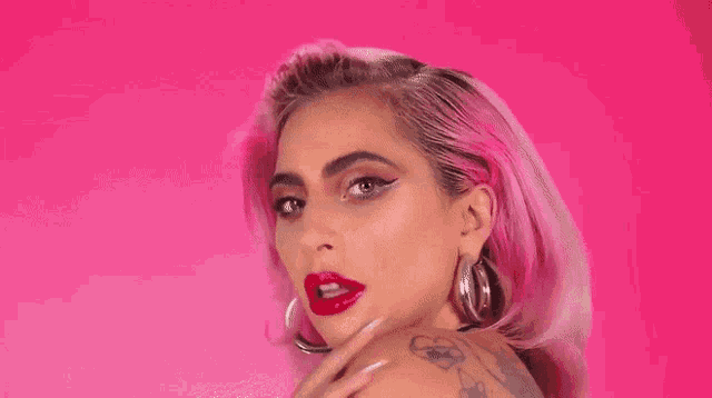 a woman with pink hair and red lipstick is wearing a black top and hoop earrings .