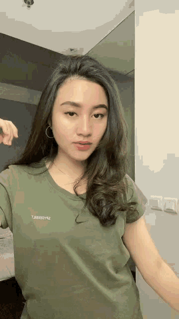 a woman wearing a green t-shirt and earrings is taking a selfie .
