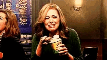 a woman in a green sweater is crying while holding a container of popcorn
