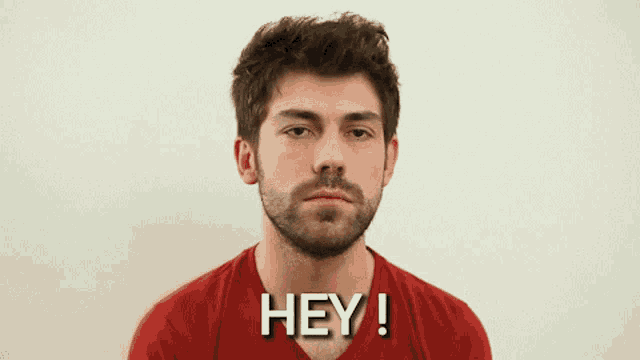 a man in a red shirt says hey in front of a white wall