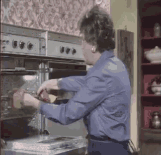 a woman in a blue shirt is putting food in an oven .