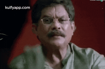 a man with glasses and a mustache is making a funny face while sitting at a table .