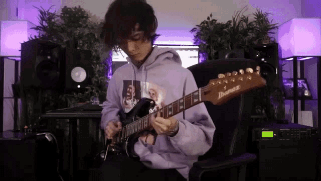 a man in a purple hoodie playing an ibanez electric guitar