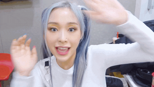 a girl with blue hair and yellow eye shadow is waving