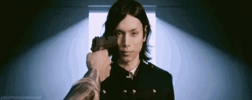 a man in a black suit is pointing a gun at another man .